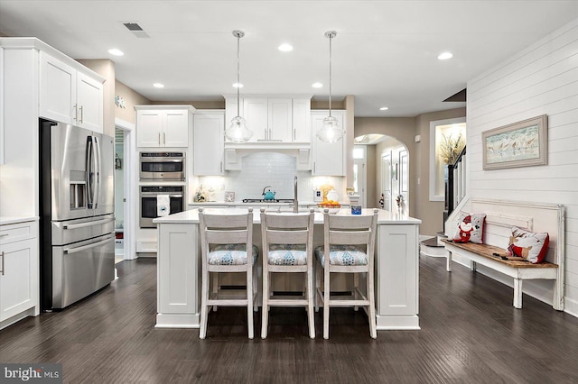 kitchen featuring a center island with sink, white cabinets, hanging light fixtures, and appliances with stainless steel finishes