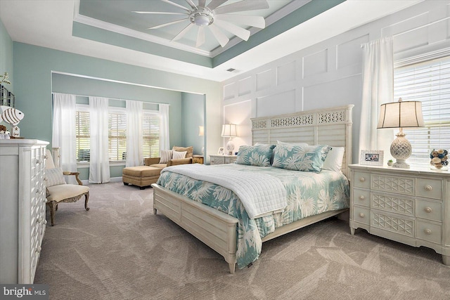 carpeted bedroom featuring a raised ceiling, ceiling fan, and crown molding