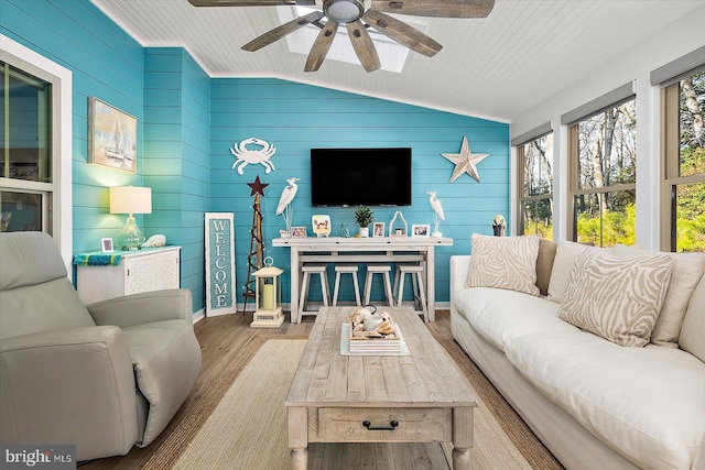 living room featuring ceiling fan, wood walls, light wood-type flooring, and vaulted ceiling