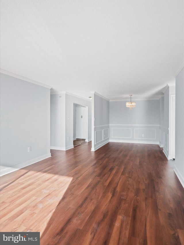 unfurnished living room featuring dark wood-type flooring, ornamental molding, and a notable chandelier