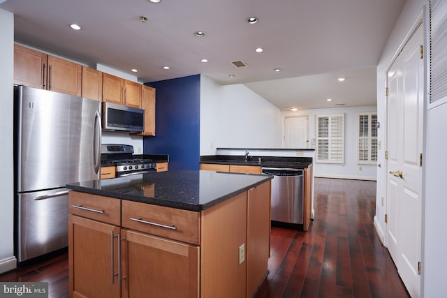 kitchen with sink, dark stone countertops, a kitchen island, dark hardwood / wood-style flooring, and stainless steel appliances