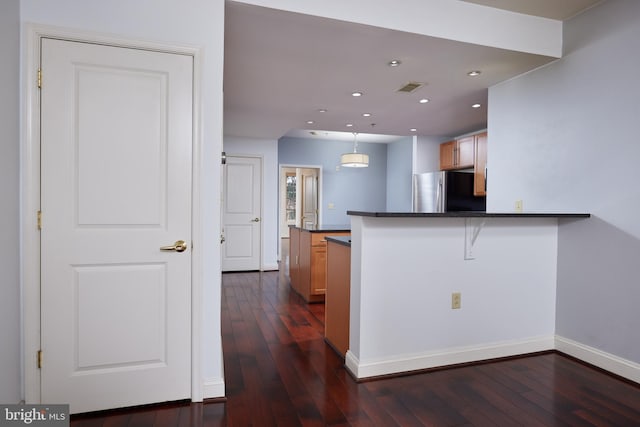 kitchen featuring hanging light fixtures, dark hardwood / wood-style flooring, a kitchen bar, kitchen peninsula, and stainless steel refrigerator