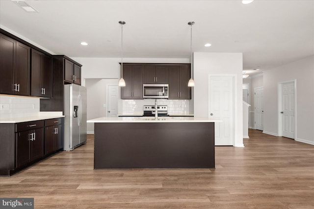 kitchen featuring appliances with stainless steel finishes, decorative light fixtures, light hardwood / wood-style flooring, and a kitchen island with sink