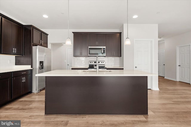 kitchen featuring light hardwood / wood-style floors, an island with sink, pendant lighting, and appliances with stainless steel finishes