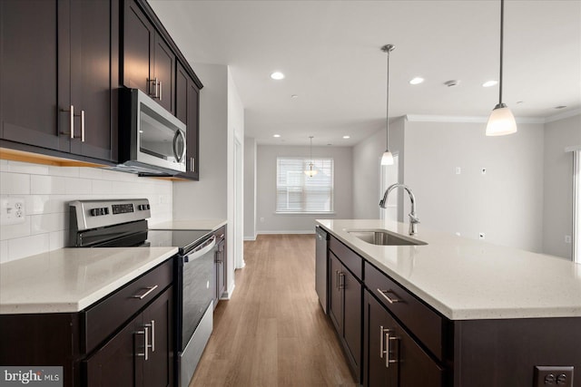 kitchen with appliances with stainless steel finishes, light wood-type flooring, ornamental molding, sink, and pendant lighting