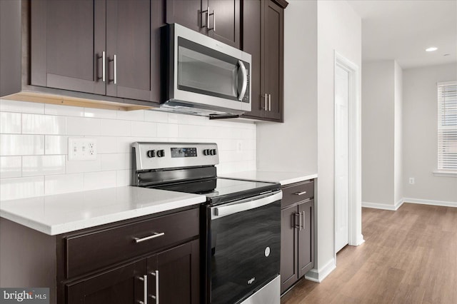 kitchen with backsplash, dark brown cabinets, light hardwood / wood-style floors, and appliances with stainless steel finishes