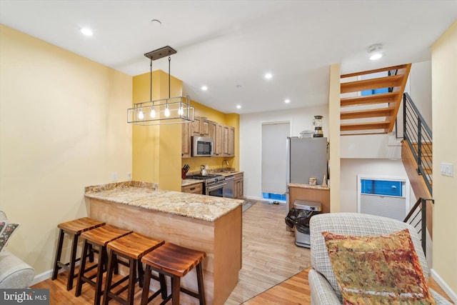 kitchen with stainless steel appliances, a kitchen breakfast bar, kitchen peninsula, decorative light fixtures, and light wood-type flooring