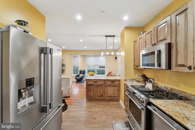 kitchen with light stone countertops, pendant lighting, stainless steel appliances, and light hardwood / wood-style floors