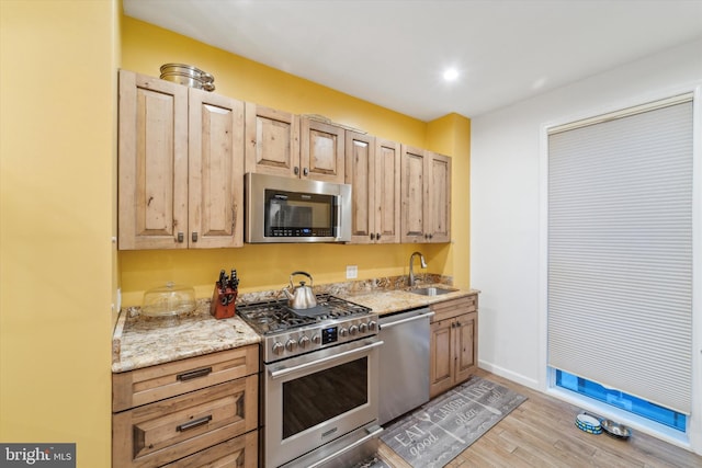 kitchen with light stone countertops, sink, light hardwood / wood-style floors, light brown cabinetry, and appliances with stainless steel finishes