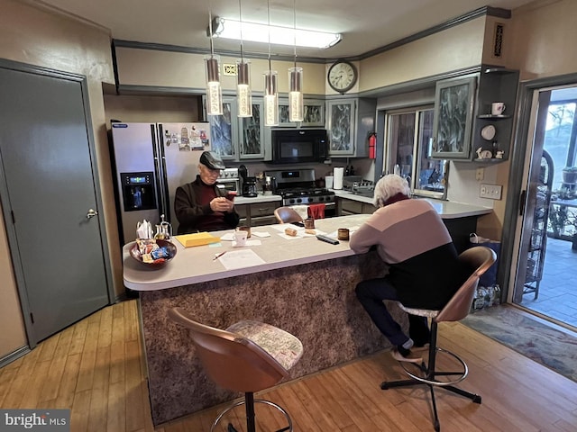 kitchen featuring a kitchen breakfast bar, crown molding, appliances with stainless steel finishes, decorative light fixtures, and light hardwood / wood-style floors