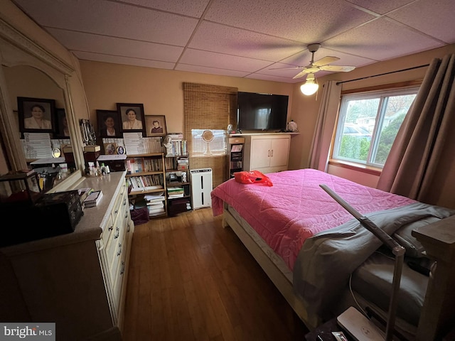 bedroom featuring wood-type flooring, a drop ceiling, and ceiling fan