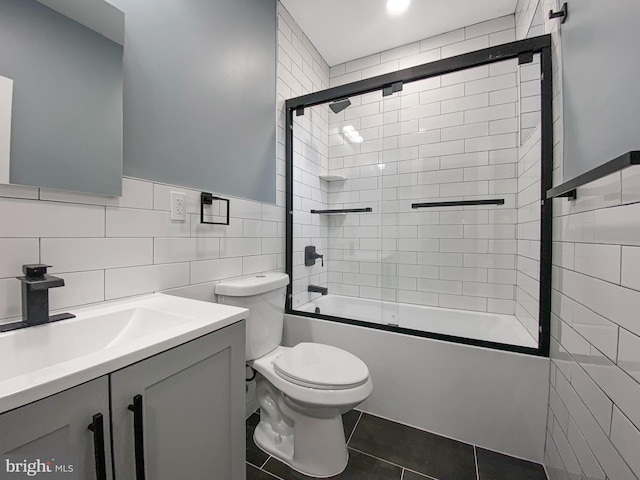 full bathroom with vanity, tile patterned floors, combined bath / shower with glass door, toilet, and tile walls