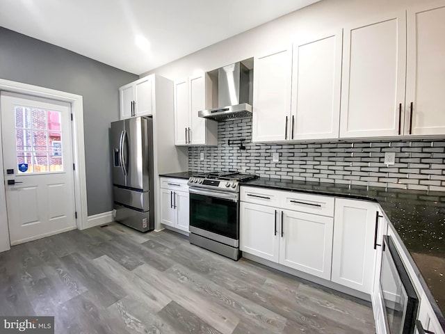 kitchen with white cabinets, wall chimney exhaust hood, wood-type flooring, and appliances with stainless steel finishes