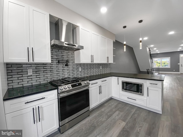 kitchen with kitchen peninsula, white cabinets, wall chimney range hood, and appliances with stainless steel finishes