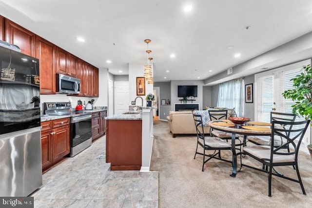 kitchen featuring light stone counters, stainless steel appliances, light colored carpet, sink, and pendant lighting