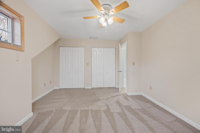 unfurnished bedroom featuring light colored carpet, vaulted ceiling, ceiling fan, and multiple closets