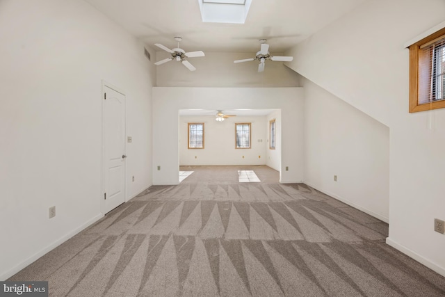 unfurnished living room with light carpet, ceiling fan, and vaulted ceiling with skylight