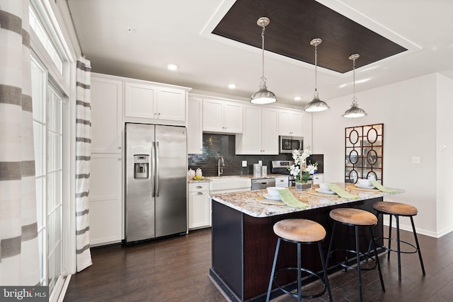 kitchen with a center island, white cabinets, a raised ceiling, hanging light fixtures, and stainless steel appliances