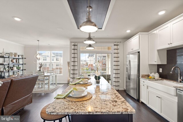 kitchen with light stone countertops, stainless steel appliances, dark hardwood / wood-style flooring, decorative light fixtures, and a kitchen island