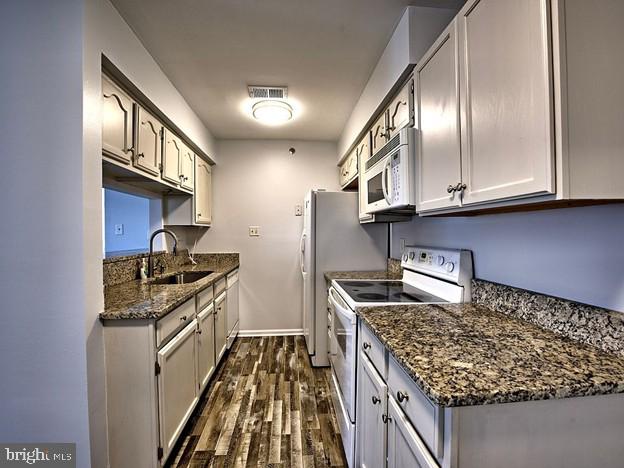 kitchen with dark hardwood / wood-style flooring, white appliances, sink, and dark stone counters