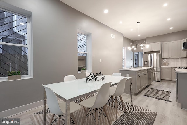 dining space with an inviting chandelier, sink, and light hardwood / wood-style flooring