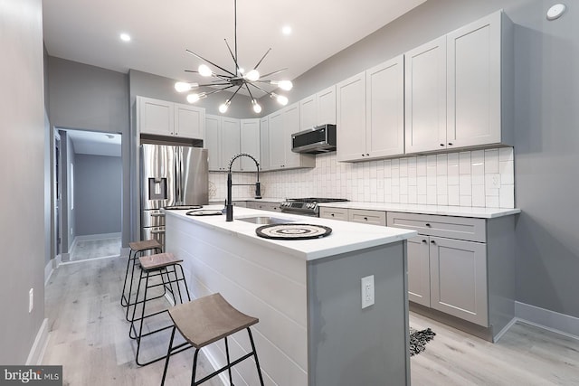 kitchen featuring appliances with stainless steel finishes, an island with sink, sink, a breakfast bar area, and backsplash