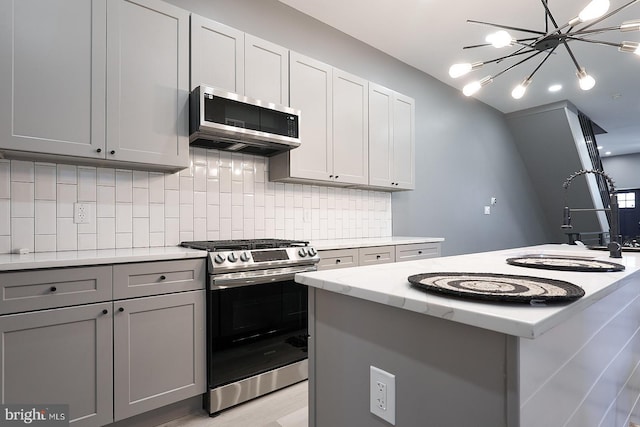 kitchen with stainless steel appliances, a kitchen island, gray cabinets, and backsplash