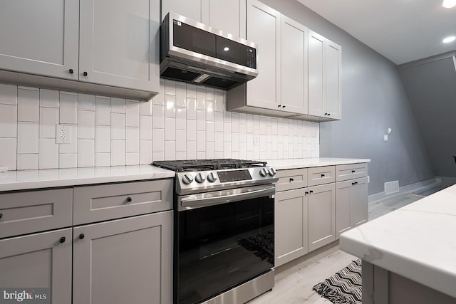 kitchen featuring extractor fan, tasteful backsplash, gray cabinetry, stainless steel appliances, and light hardwood / wood-style flooring