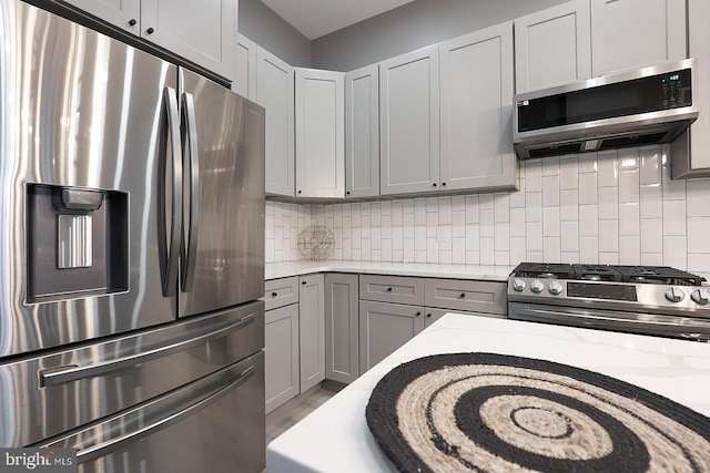 kitchen with gray cabinets, appliances with stainless steel finishes, decorative backsplash, hardwood / wood-style flooring, and light stone countertops