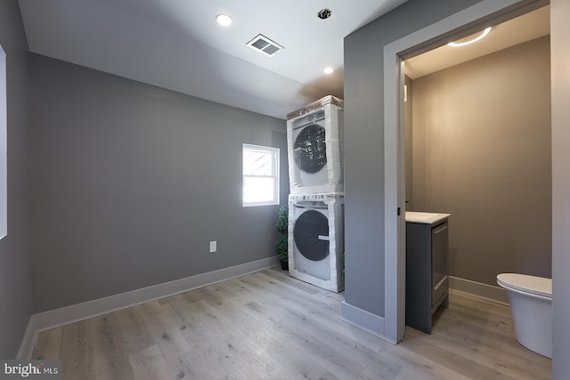 clothes washing area with stacked washer / drying machine and light wood-type flooring