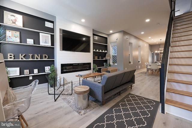 living room featuring built in shelves, wood-type flooring, a large fireplace, and a chandelier