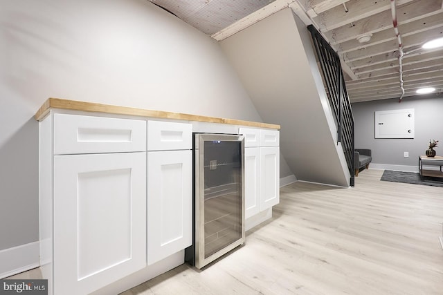 kitchen with vaulted ceiling, beverage cooler, light wood-type flooring, and white cabinets