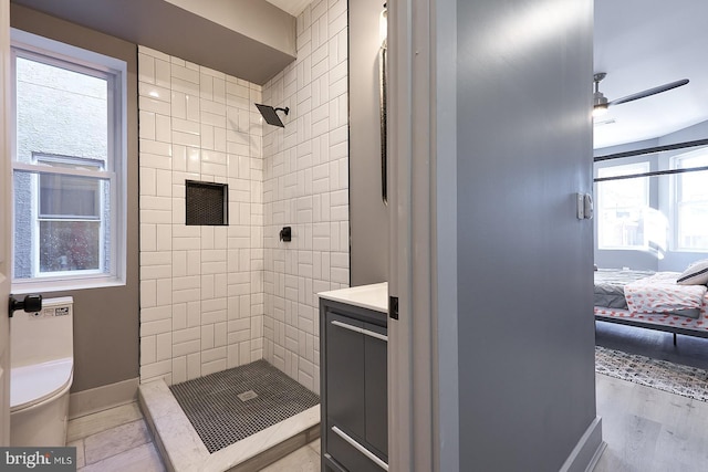 bathroom featuring ceiling fan, vanity, toilet, and a tile shower