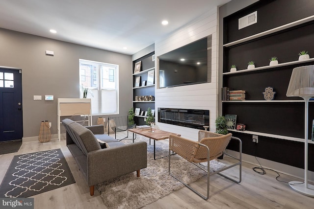 living room with built in shelves, light hardwood / wood-style flooring, and a large fireplace