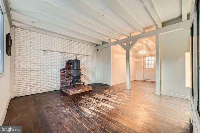 unfurnished living room featuring hardwood / wood-style flooring, lofted ceiling with beams, and brick wall