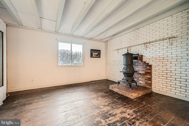 unfurnished living room with beam ceiling, a wood stove, dark wood-type flooring, and brick wall