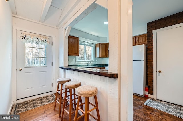 kitchen featuring wood walls, dark wood-type flooring, white fridge, kitchen peninsula, and a breakfast bar area