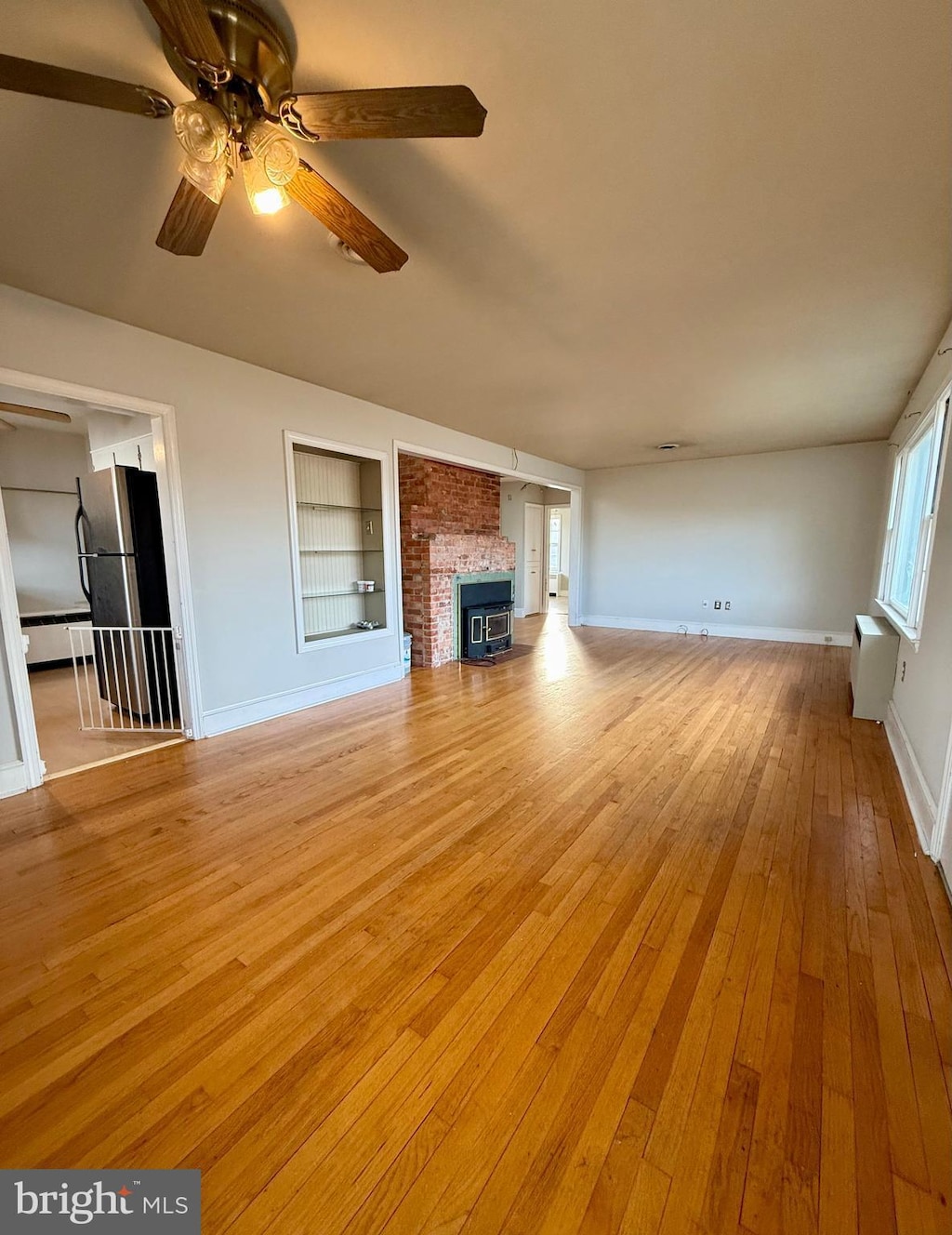 unfurnished living room with ceiling fan, a baseboard radiator, a brick fireplace, built in features, and light wood-type flooring