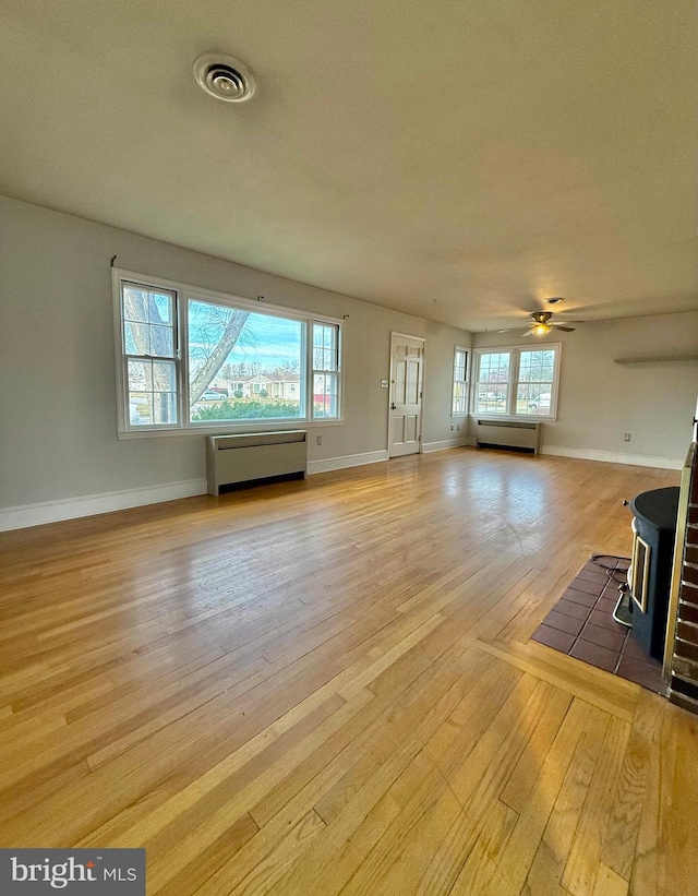 unfurnished living room with ceiling fan, light hardwood / wood-style floors, a wood stove, and a wealth of natural light