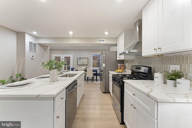 kitchen featuring light stone counters, white cabinets, stainless steel appliances, and wall chimney range hood