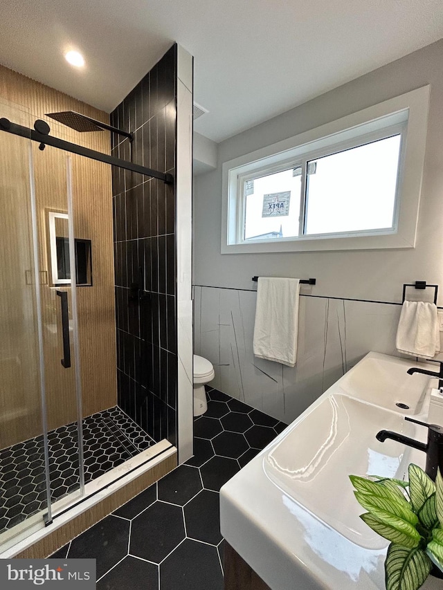 bathroom with tile patterned floors, toilet, a shower with shower door, and tile walls