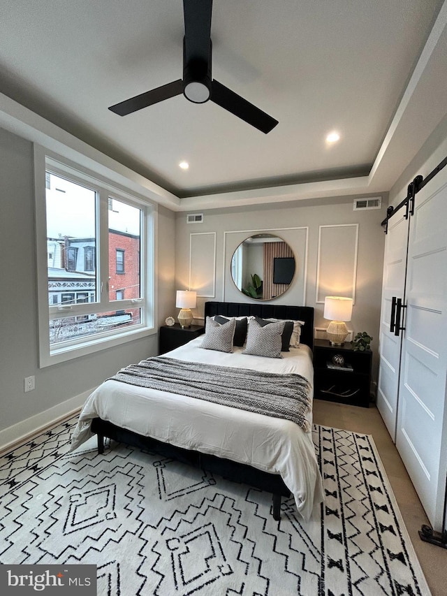 bedroom with a barn door, a raised ceiling, and ceiling fan