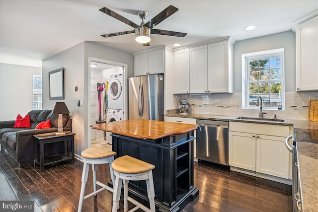 kitchen featuring light stone countertops, sink, stacked washing maching and dryer, dark hardwood / wood-style floors, and appliances with stainless steel finishes