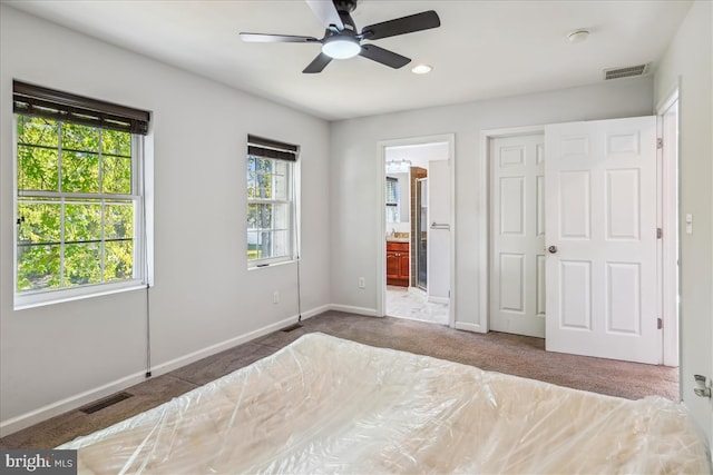 unfurnished bedroom featuring dark colored carpet, ensuite bathroom, and ceiling fan