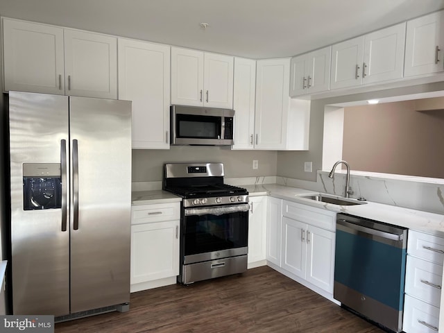 kitchen with light stone countertops, appliances with stainless steel finishes, dark hardwood / wood-style flooring, sink, and white cabinetry