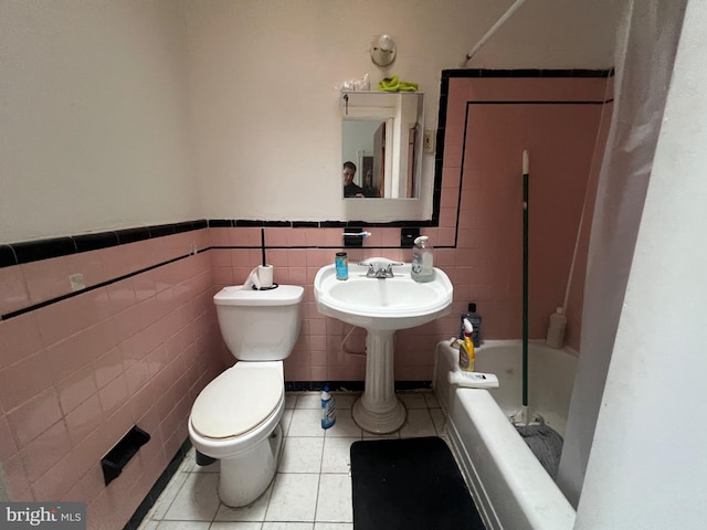 bathroom with toilet, bathing tub / shower combination, tile patterned floors, and tile walls