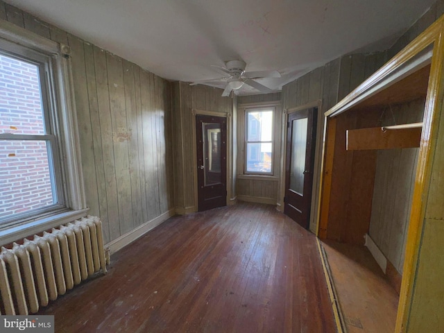 interior space with radiator heating unit, wooden walls, and dark wood-type flooring