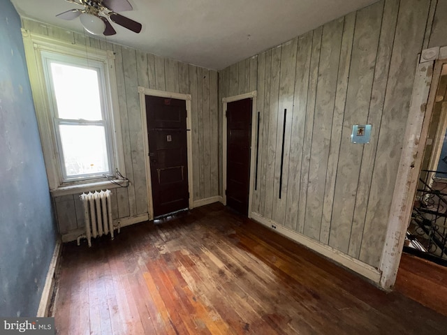 spare room featuring wooden walls, radiator heating unit, ceiling fan, and dark wood-type flooring