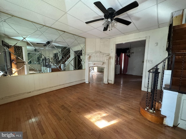 unfurnished living room featuring hardwood / wood-style floors, a drop ceiling, radiator heating unit, and ceiling fan with notable chandelier