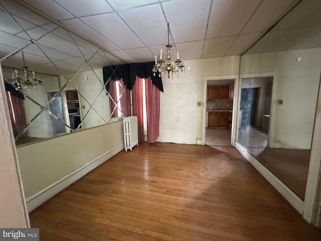 unfurnished dining area with radiator heating unit, a paneled ceiling, a notable chandelier, and wood-type flooring